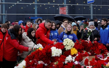 A group of young Russians lay more flowers on a huge pile of roses, on a grey day